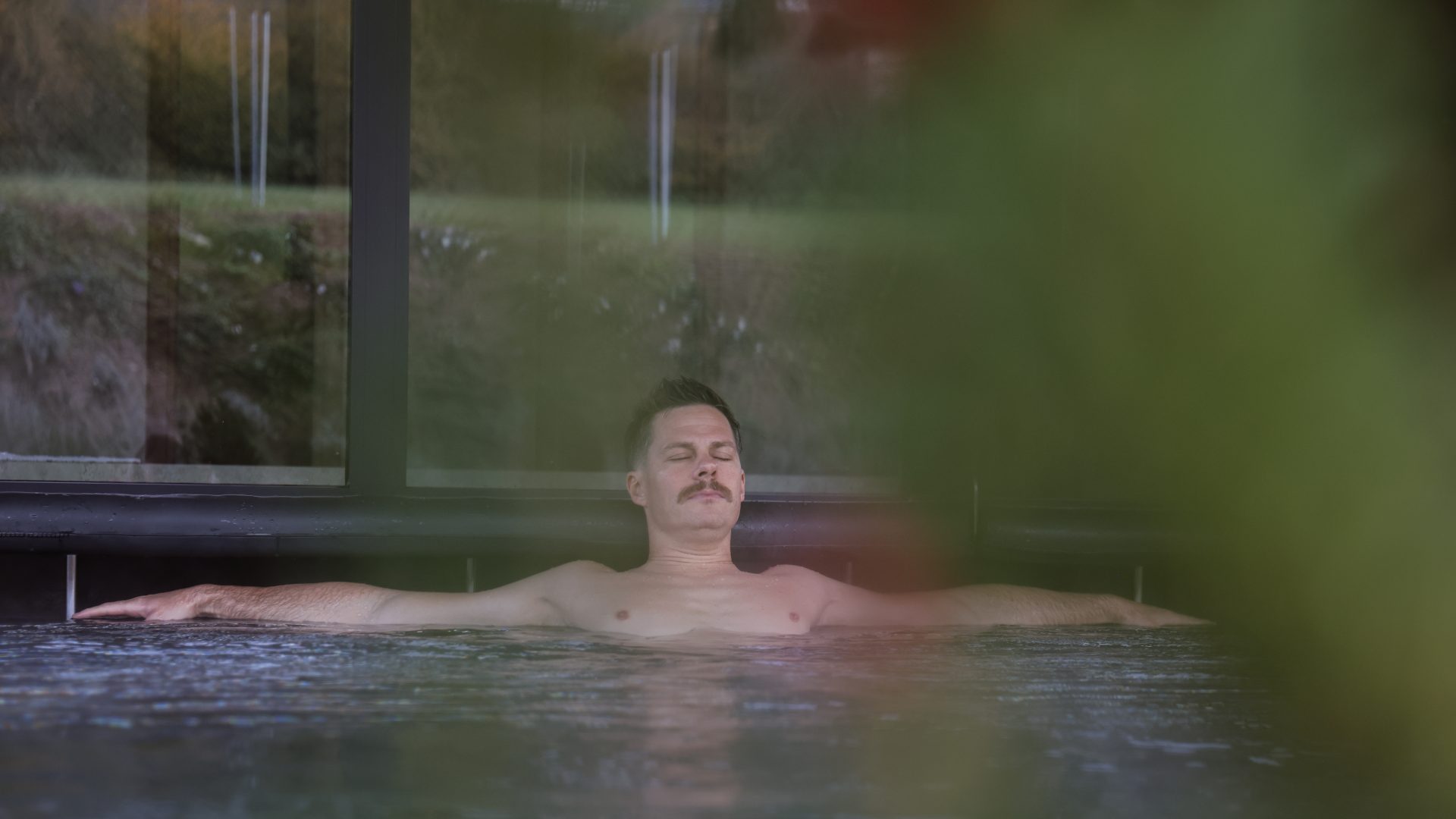 Entspannter Mann im Wellnessbad mit Blick auf die Natur in Tiroler Wellnesshotels.