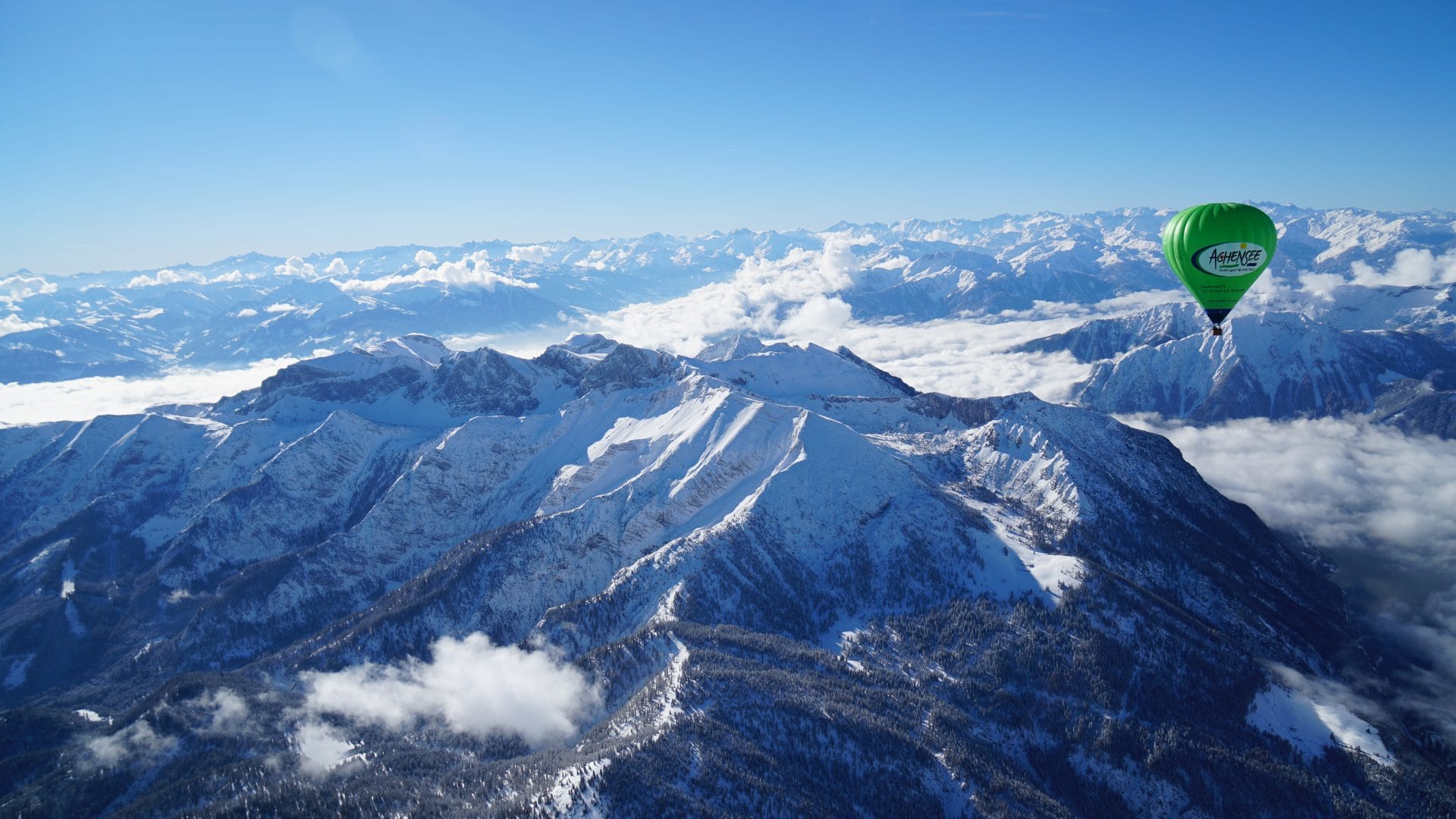 Heißluftballon fliegt über verschneite Tiroler Alpen bei klarer Wintersonne.