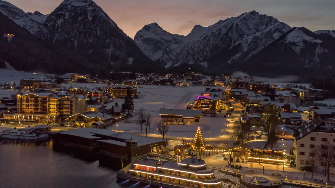 Stimmungsvolle Winternacht in Tirol, Wellnesshotels mit Blick auf schneebedeckte Berge und festlich beleuchtete Häuser.