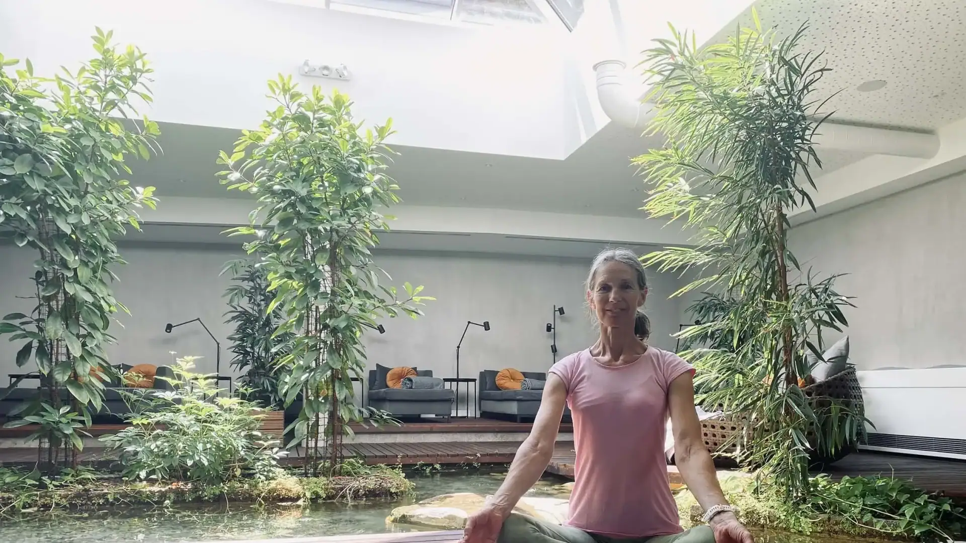 Entspannte Frau bei Yoga in einem modernen Wellnesshotel mit Indoor-Garten und Pflanzen.