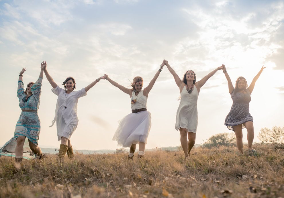 Frauen tanzen im Freien, halten sich an den Händen, genießen die Natur und das schöne Wetter.
