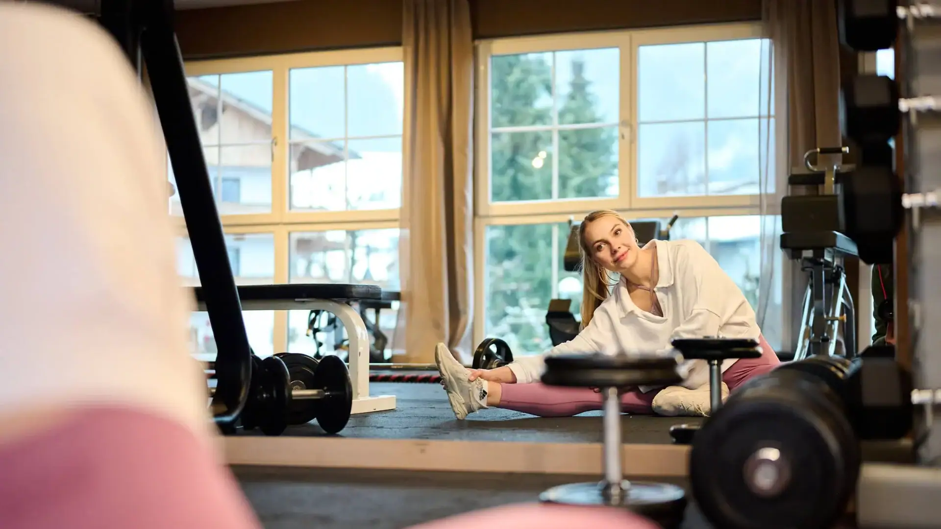 Frau beim Dehnen im Fitnessraum mit Bergblick, Wellnesshotel Tirol.