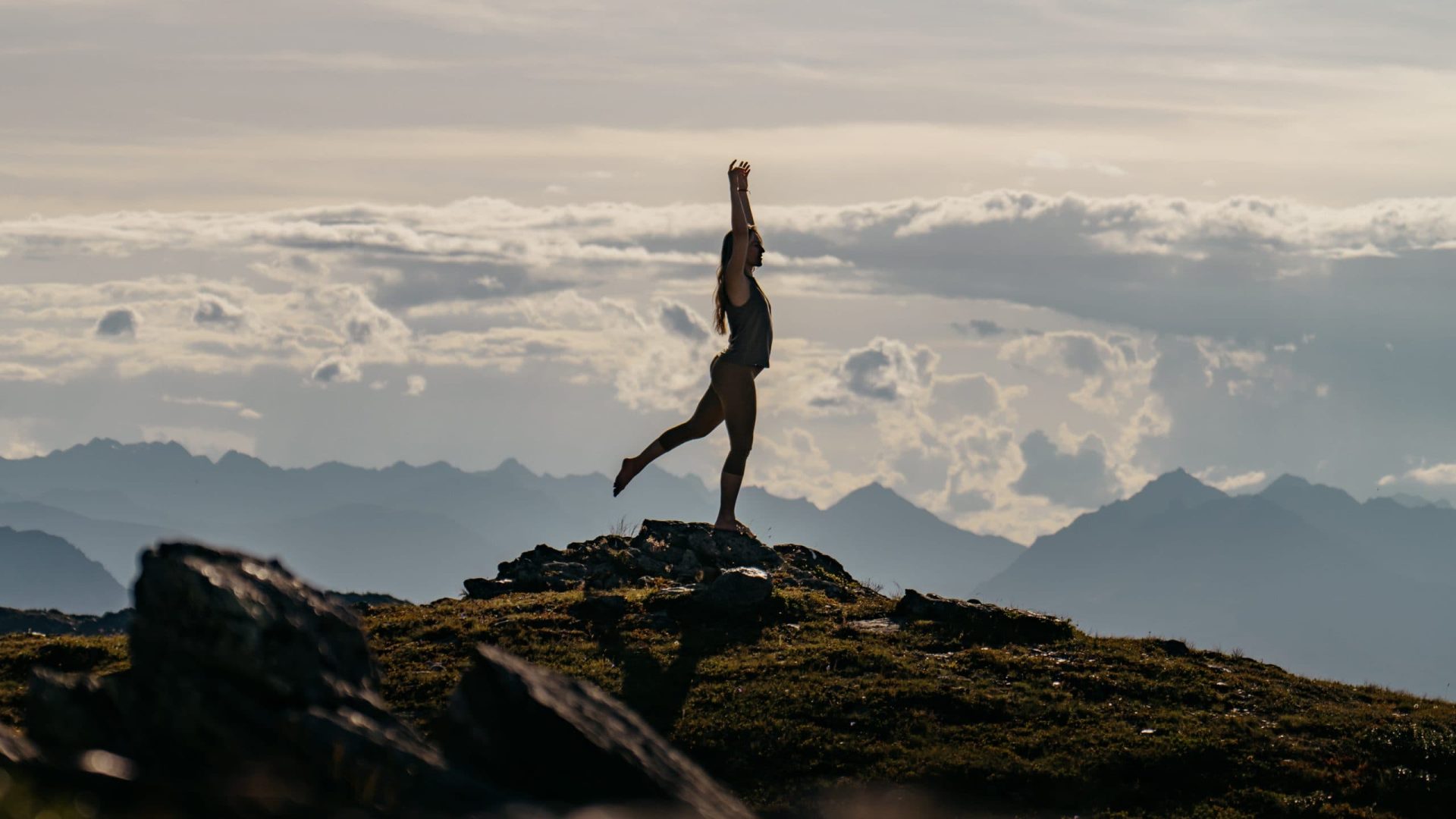 Frau macht Yoga auf einem Berggipfel bei Sonnenuntergang in Tirol, Wellness und Natur genießen.