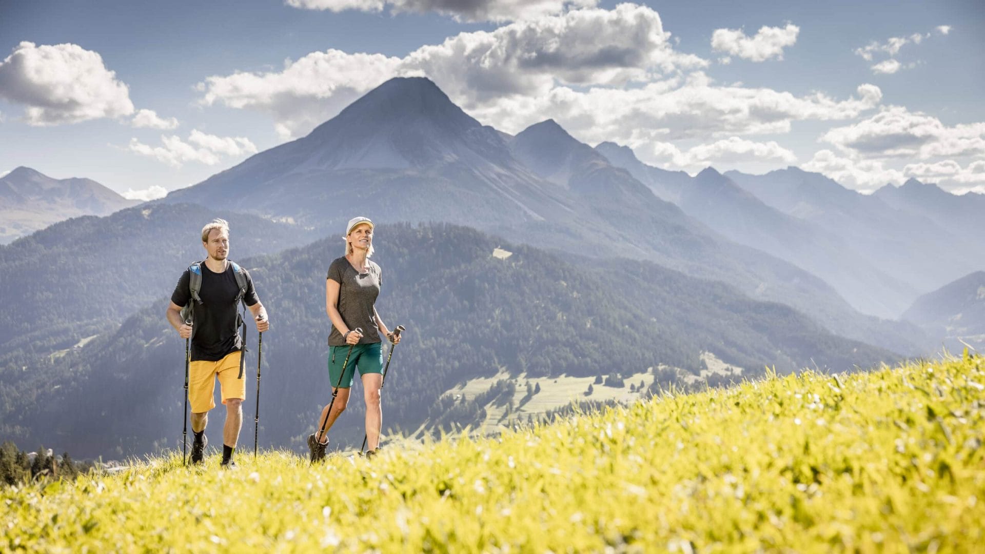 Zwei Wanderer auf einer Bergwiese mit Blick auf die Tiroler Alpen.
