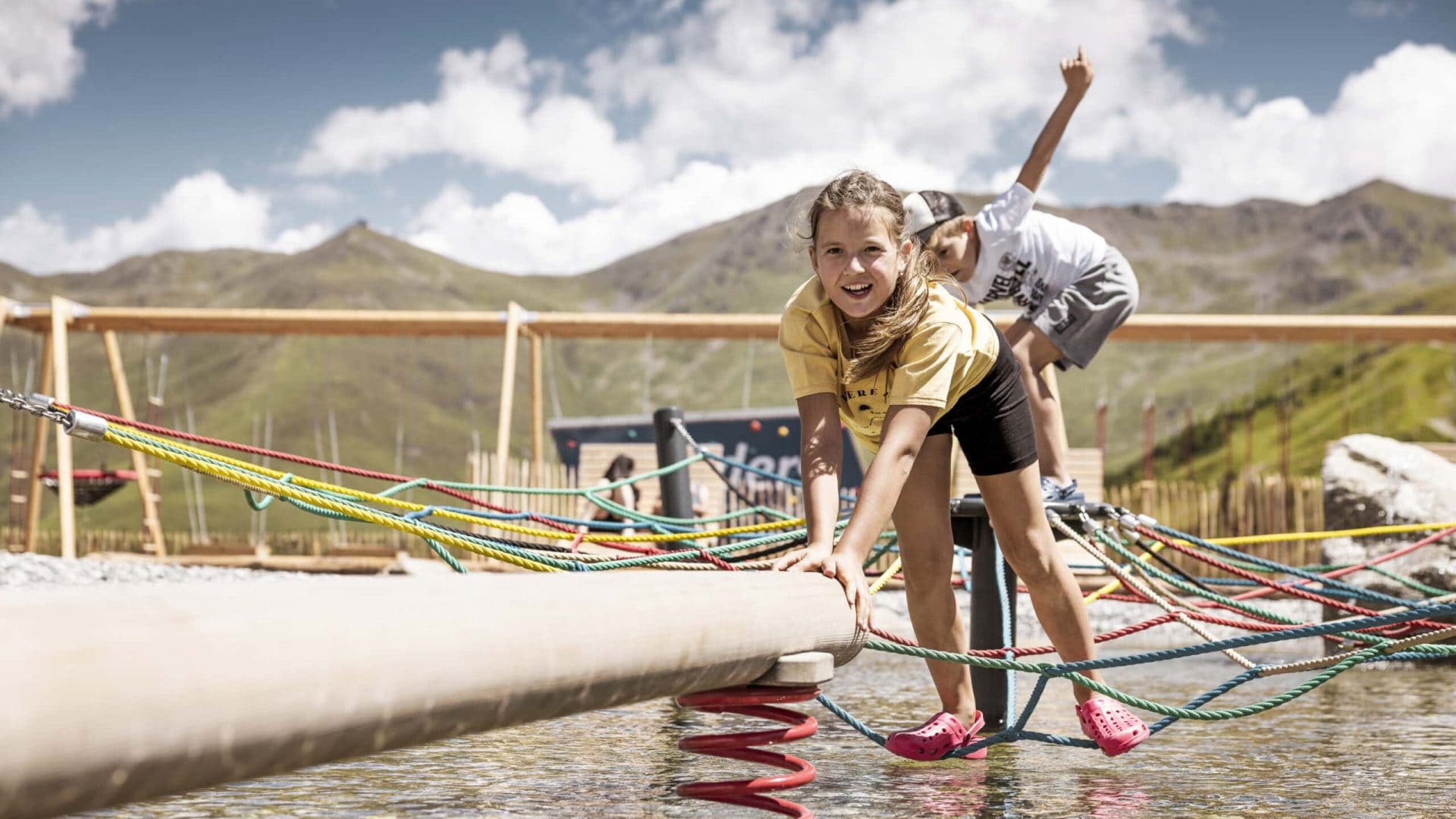 Kinder spielen im Wasserpark mit Seilbrücke in den Tiroler Bergen.