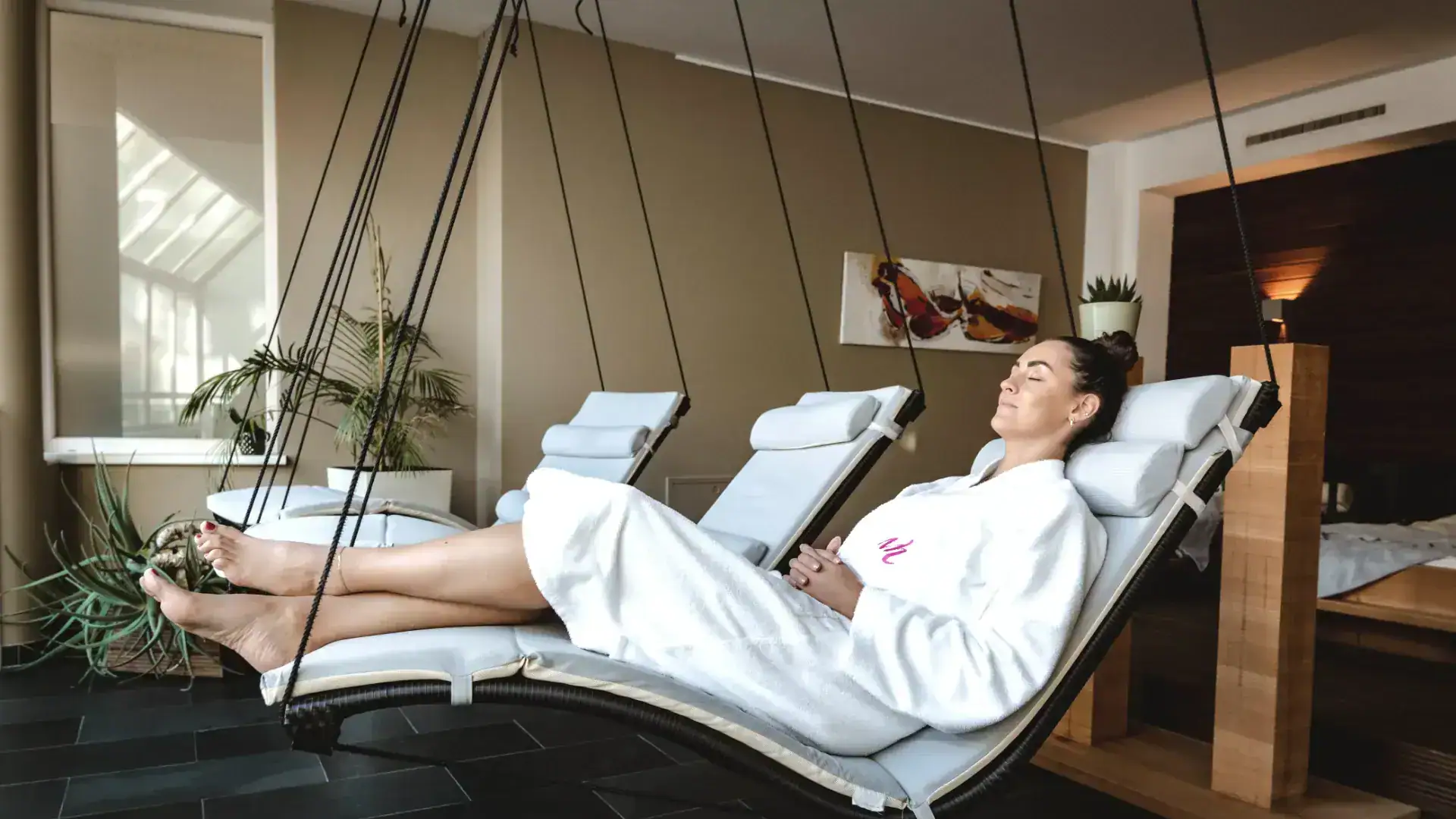 Frau entspannt auf einer Relaxliege im Wellnessbereich mit Hängematte.